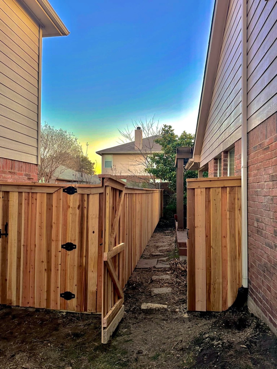 New cedar wood privacy fence with a matching gate installed in a Rockwall County, Texas backyard at sunset