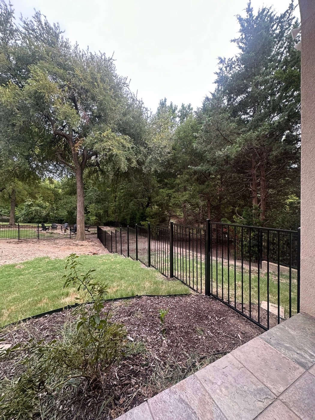 Black ornamental iron fence running down a wooded hillside